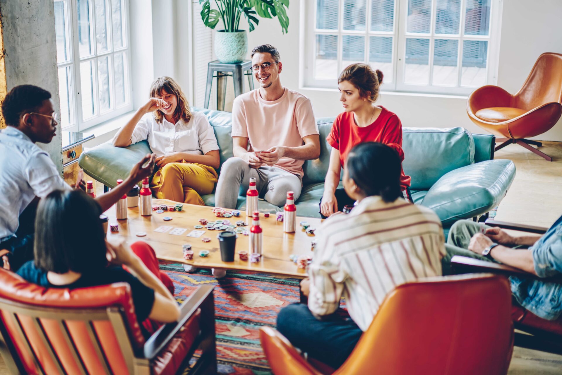 7 junge Menschen sitzen zum Pokern zusammen und halten ihre Poker-Karten auf der Hand